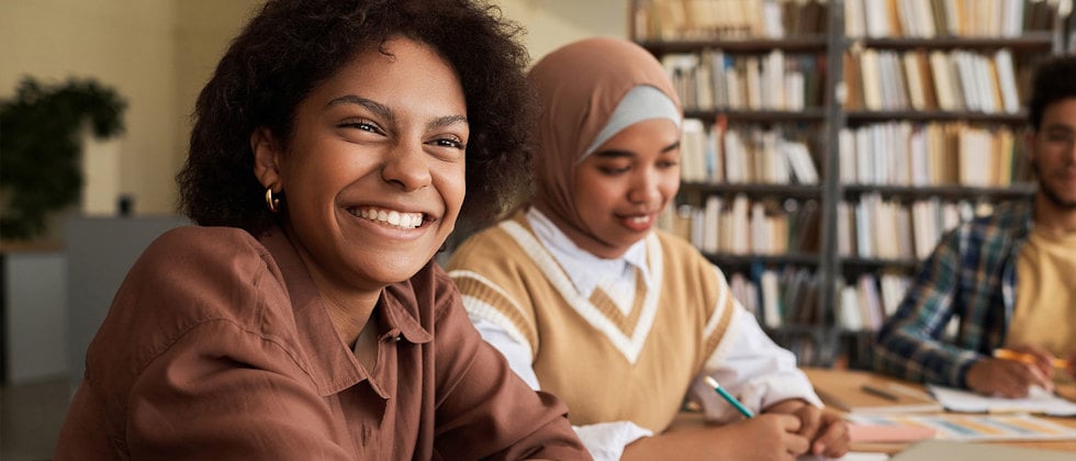 En genrebild av tre elever som sitter med papper framför sig på bordet, en bär hijab.