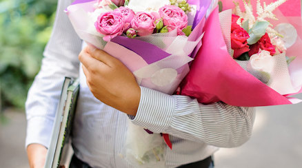 En man i skjorta med böcker under ena armen och två blombuketter